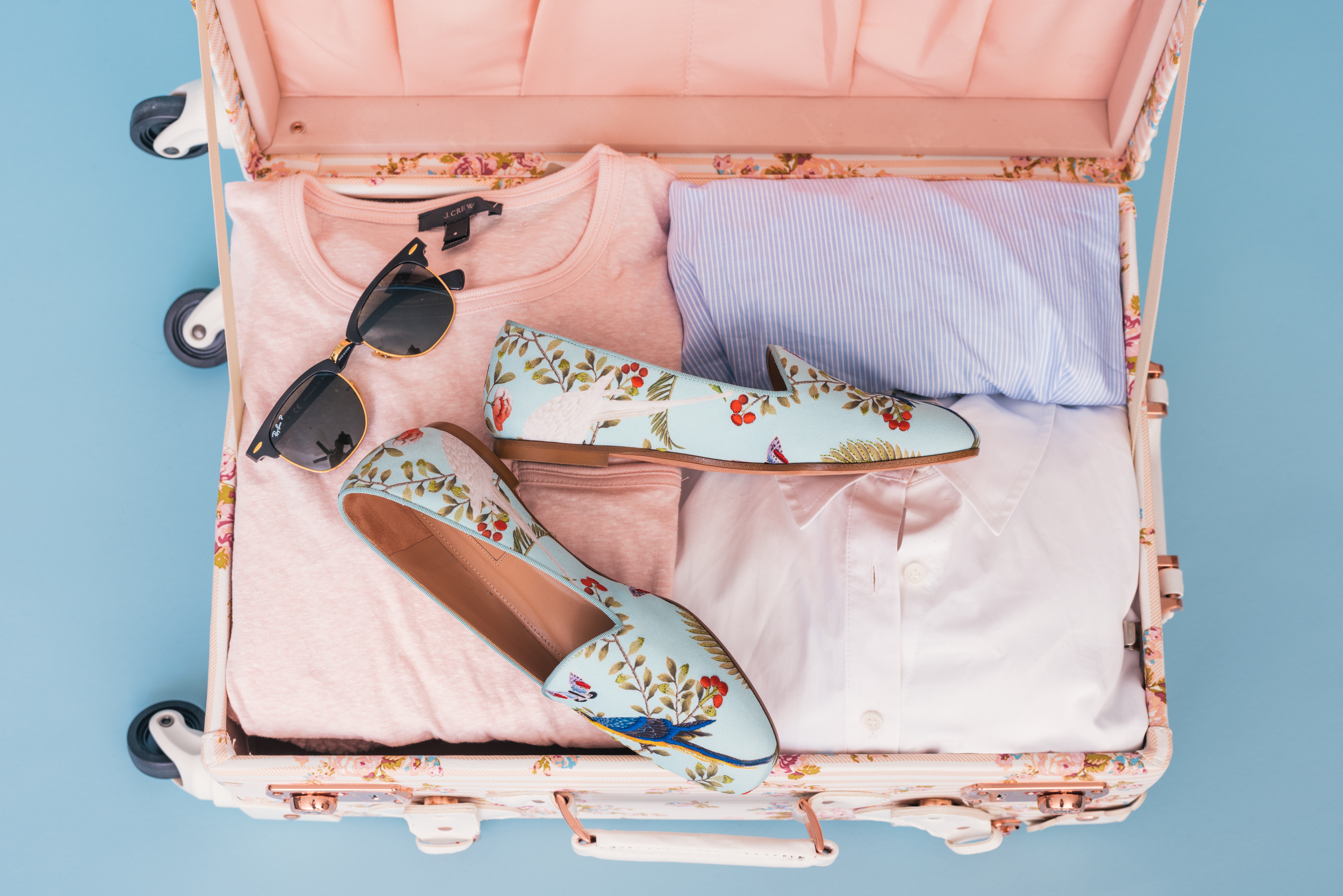 roze koffer gevuld met kleding, zonnebril en bloemetjes schoenen